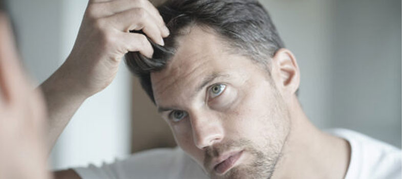 Mann, der seinen Haaransatz im Spiegel ansieht, steht für Regenera Activa® gegen Haarausfall