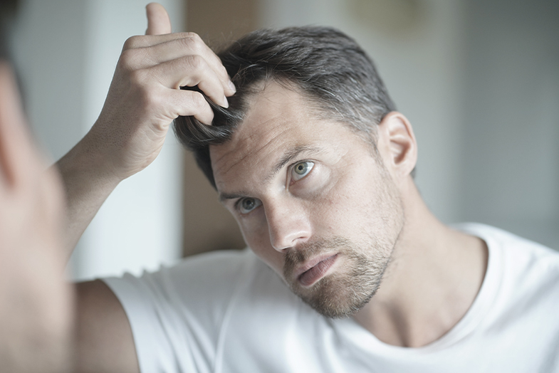 Mann, der seinen Haaransatz im Spiegel ansieht, steht für Regenera Activa® gegen Haarausfall